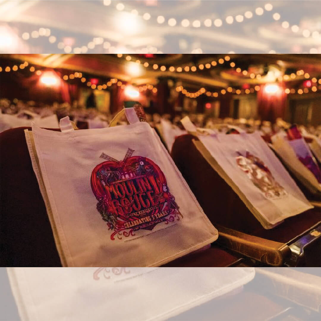 Sacs promotionnels Moulin Rouge distribués aux spectateurs dans une salle de théâtre.