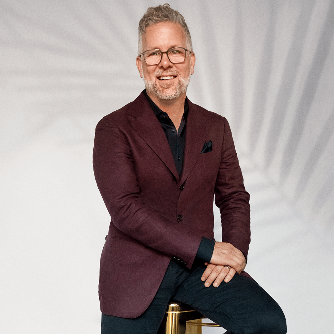 Christian Quenneville sitting on a gold stool, smiling confidently.