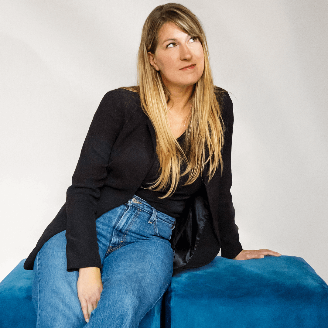 Christine Lavergne sitting on two blue cubes, looking up thoughtfully.