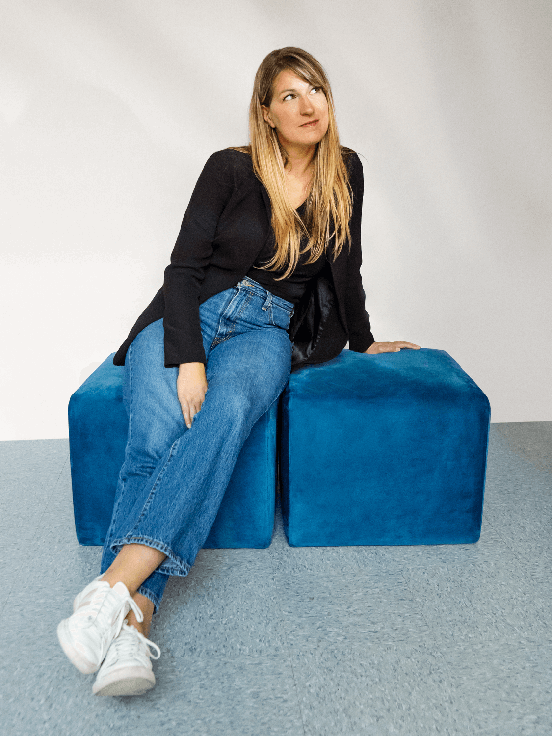 Christine Lavergne sitting on two blue cubes, looking up thoughtfully.