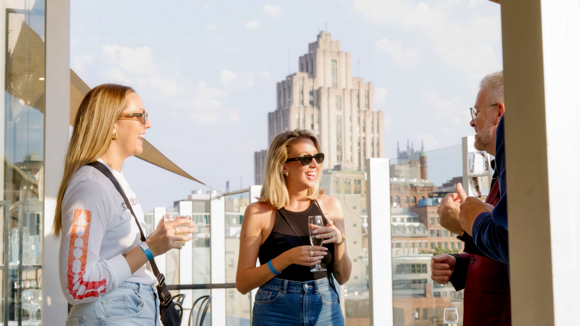 Three people chatting on a sunny terrace in Montreal with city buildings in the background